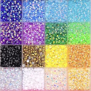 Puede incluir: Un organizador de pl&aacute;stico transparente lleno de peque&ntilde;os pedrer&iacute;a iridiscente de varios colores. La pedrer&iacute;a est&aacute; dispuesta en compartimentos cuadrados, mostrando una gama de colores que incluyen azul, verde, morado, dorado y rosa. Ideal para proyectos de manualidades y embellecimiento.