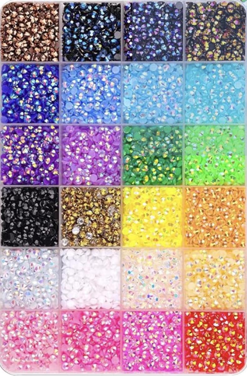 Puede incluir: Un organizador de pl&aacute;stico transparente lleno de peque&ntilde;os pedrer&iacute;a iridiscente de varios colores. La pedrer&iacute;a est&aacute; dispuesta en compartimentos cuadrados, mostrando una gama de colores que incluyen azul, verde, morado, dorado y rosa. Ideal para proyectos de manualidades y embellecimiento.