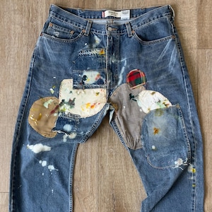 May include: Blue denim jeans with patches of different fabrics and paint splatters. The patches include plaid, brown, and white fabrics.