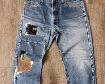 May include: Blue denim jeans with white paint splatters and patches of fabric. The jeans have a relaxed fit and a straight leg.