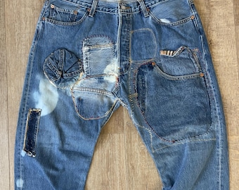May include: Blue denim jeans with multiple patches sewn on the front. The patches are made of different shades of blue denim and are sewn in a variety of patterns.