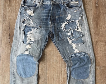 May include: Distressed blue denim jeans with multiple patches and repairs. The jeans have a faded look and are ripped in several places.