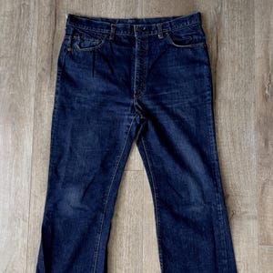 Puede incluir: Vaqueros de mezclilla azul oscuro con un diseño clásico de cinco bolsillos. Los vaqueros tienen una pernera recta con un ligero acampanado en el dobladillo. Los vaqueros están hechos de un material de mezclilla resistente y cuentan con cierre de botón y cremallera.