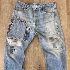 Może przedstawiać: Jasnoniebieskie dżinsy z wieloma łatami i naprawami. Dżinsy mają wyblakły wygląd i są zniszczone.