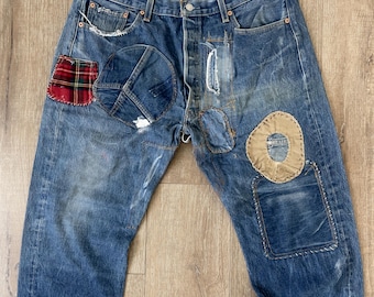 May include: Blue denim jeans with multiple patches, including a plaid patch, a brown leather patch, and a blue denim patch.