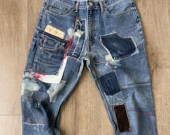 May include: Blue denim jeans with multiple patches of different fabrics and colors, including brown corduroy, white cotton, and blue denim. The jeans have a distressed look with faded areas and visible stitching.
