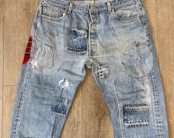 May include: Light blue denim jeans with multiple patches sewn on. The patches are made of different fabrics and colors, including red, white, and blue. The jeans have a faded look and are distressed.