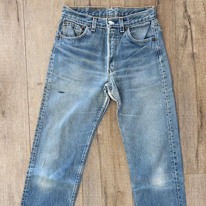 May include: Faded blue denim jeans with a button fly and classic five-pocket design. The jeans show signs of wear, with lighter patches and subtle distressing. A timeless wardrobe staple.