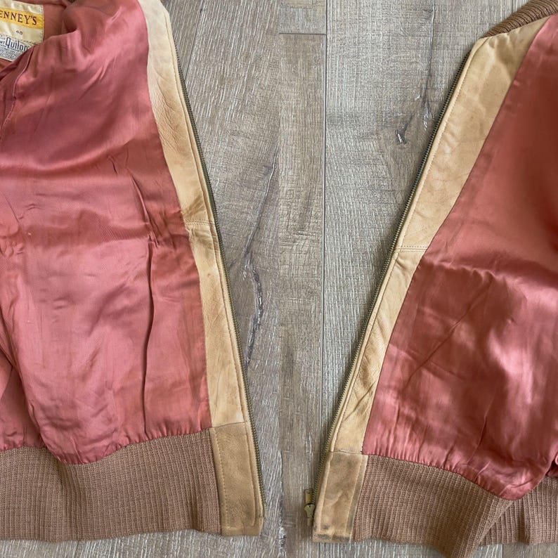 May include: A vintage jacket with a pink satin lining, tan leather accents, and a brown ribbed knit hem. The jacket has a zipper closure and a tag that reads "Kenney's".