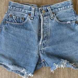 Op de afbeelding: Lichtblauwe denim shorts met een rafelige zoom. De shorts hebben vijf zakken en een knoopsluiting.