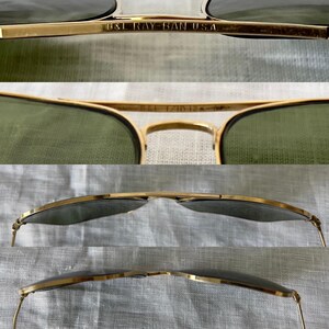 May include: Close-up of gold-rimmed sunglasses with green lenses. The text "B&L RAY-BAN USA" is visible on the frame. The sunglasses have a classic aviator style. The lenses are a muted green color, and the frames are a shiny gold.