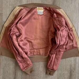 May include: A vintage brown suede jacket with a pink satin lining. The jacket features a ribbed collar and cuffs, and a tag that reads "PENNEYS". The jacket is laid flat, showcasing its interior and construction.