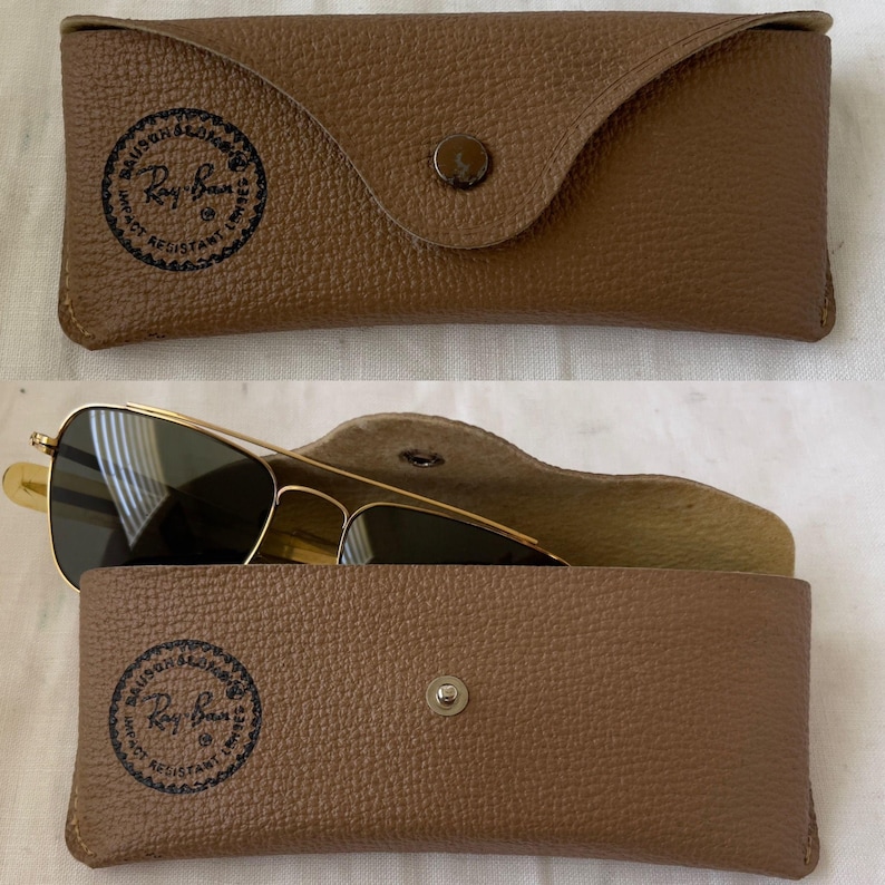 Puede incluir: Un estuche de gafas de cuero marr&oacute;n con cierre de bot&oacute;n a presi&oacute;n, con el logotipo de Ray-Ban. El estuche est&aacute; abierto, revelando gafas de sol con montura dorada y lentes oscuras.
