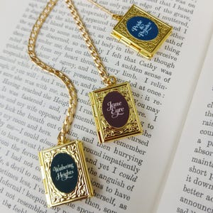 May include: Gold-colored book pendant necklaces with chains. Each pendant features a different classic novel title: "Pride & Prejudice," "Jane Eyre," and "Wuthering Heights." The pendants have an oval-shaped center with the book title.
