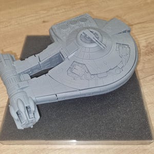 Könnte beinhalten: Ein graues Plastikmodell eines Raumschiffs mit einem runden Cockpit und einem langen, dünnen Körper. Das Modell steht auf einem grauen Sockel.