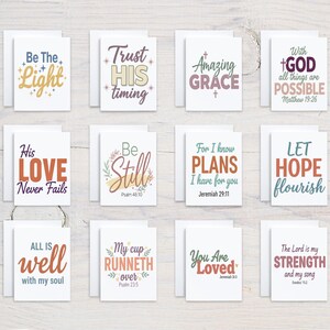 May include: A set of twelve white greeting cards featuring various inspirational quotes and religious phrases in colorful typography, including Be The Light, Trust HIS timing, Amazing Grace, With GOD all things are POSSIBLE, His LOVE Never Fails, Be Still, For I know PLANS I have for you, LET HOPE flourish, ALL IS well with my soul, My cup RUNNETH over, You Are Loved, and The Lord is my STRENGTH and my song.