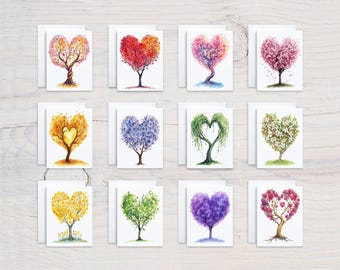 May include: Twelve watercolour paintings of heart-shaped trees in various colours, including red, pink, yellow, green, blue, and purple. Each painting is on a white card with a white border.