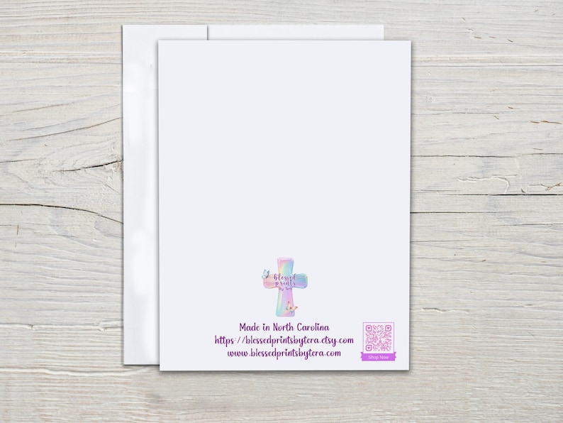 May include: A white greeting card with a pastel cross design and the text "Made in North Carolina". The card includes a website address and a QR code. The card is placed on a light wood surface.