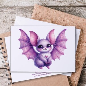 May include: A greeting card featuring a cute, cartoon bat with large eyes and purple wings. The bat has a heart on its chest. The card is on top of a white envelope, a spiral notebook, and a corkboard.