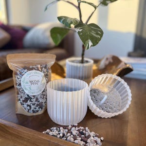 Könnte beinhalten: Ein weißer Plastiktopf mit Drainagelöchern, ein weißer Plastiktopf mit geripptem Design und ein Beutel mit weißer, brauner und roter Erde. Der Beutel trägt ein Etikett mit der Aufschrift "Monk Pon".