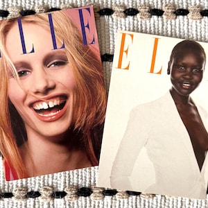 May include: Two vintage ELLE magazine covers. One features a smiling blonde woman with the magazine title in large blue letters. The other cover shows a woman in a white blazer with the magazine title in orange letters.