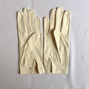 May include: A pair of cream-colored leather gloves. The gloves have a classic design with a button closure at the wrist. The fingers are individually stitched, and the gloves appear to be in good condition.