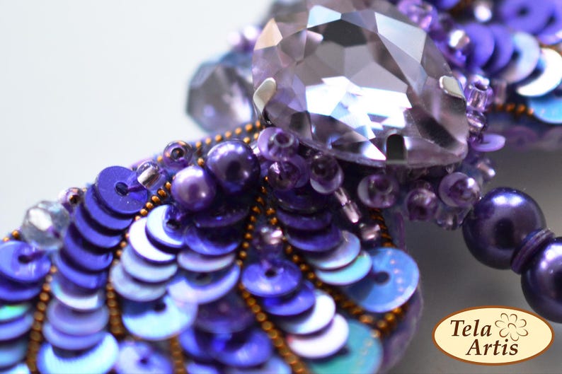 May include: A purple and blue beaded dragonfly brooch with a large iridescent crystal in the center. The dragonfly's wings are made of sequins and beads.