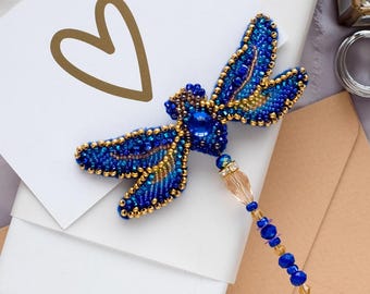 May include: A blue and gold beaded dragonfly brooch with a crystal pendant and a beaded tail.