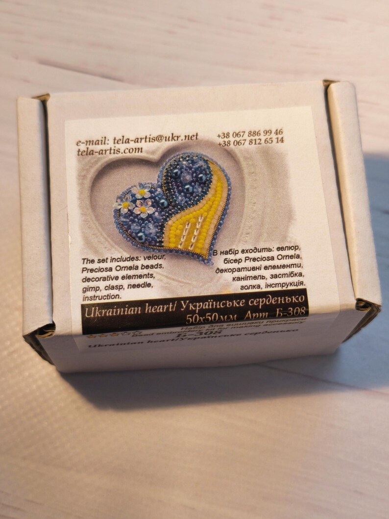 May include: A blue and yellow beaded heart with a floral design. The heart is 50x50mm and is labeled "Ukrainian heart/ Українське серденько".
