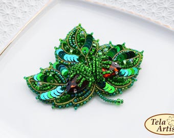 May include: A green and brown beaded brooch in the shape of a butterfly. The brooch is made with sequins and beads and has a detailed design.