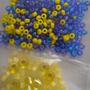 May include: A close-up of two bags of seed beads. One bag contains blue and yellow seed beads, and the other bag contains yellow seed beads.