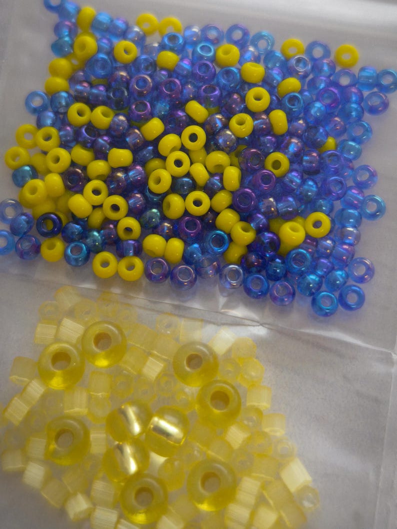May include: A close-up of two bags of seed beads. One bag contains blue and yellow seed beads, and the other bag contains yellow seed beads.