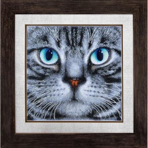 May include: Close-up of a gray tabby cat's face with bright blue eyes. The cat's nose is pink and its whiskers are visible. The image is made up of small, colorful beads.