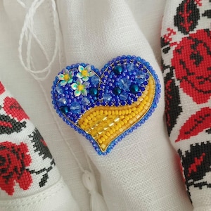 May include: A heart-shaped beaded brooch with blue and yellow beads. The brooch is decorated with small yellow flowers.