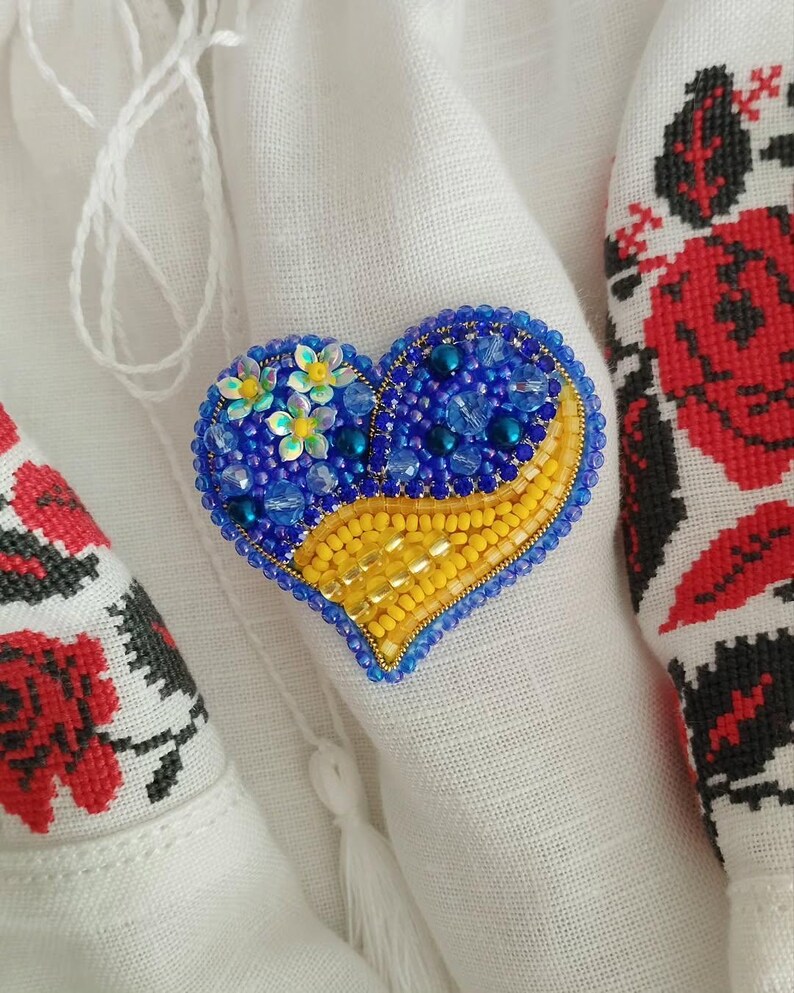 May include: A heart-shaped beaded brooch with blue and yellow beads. The brooch is decorated with small yellow flowers.