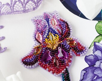 May include: A beaded flower brooch in shades of purple, pink, red, and yellow. The flower is made with small beads and rhinestones, and it has a green stem.