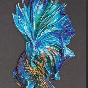 May include: A beaded artwork depicting a Betta fish, with a striking display of blues, greens, and gold. The fish's fins and body are intricately detailed with beads, creating a textured effect. The background is a solid dark grey.