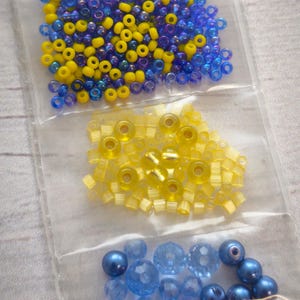 May include: Three bags of beads in blue and yellow colors. The first bag contains small round blue and yellow beads. The second bag contains small square yellow beads. The third bag contains larger round blue beads.