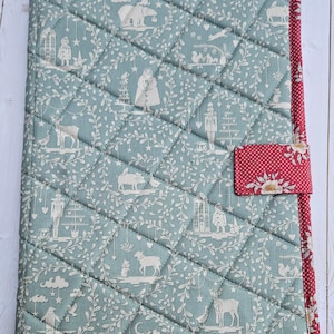 May include: Quilted journal cover with a light blue background and a repeating pattern of white winter-themed illustrations. The cover is bordered with red fabric featuring white polka dots and a red closure.