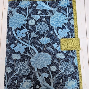 May include: A rectangular fabric cover featuring a dark navy blue background with a repeating pattern of light blue flowers and foliage. The cover is edged with a textured olive green border and includes a matching olive green fabric tab closure.