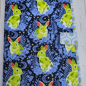 May include: A quilted fabric notebook cover featuring a repeating pattern of green rabbits with red ears on a navy blue background with blue floral and gold star accents. The cover has a button closure and a light blue floral border.