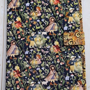May include: A rectangular quilted fabric cover featuring a dark navy background with a repeating pattern of children holding lanterns, small white rabbits, butterflies, and colorful flowers. The edges are finished with a gold swirl patterned border.