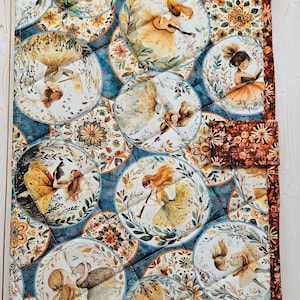 May include: A quilted fabric cover featuring a repeating pattern of circular illustrations depicting figures playing musical instruments, reading, and interacting with animals, set against a deep blue background with orange floral borders.