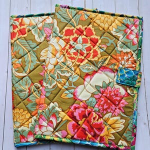 May include: Two rectangular quilted fabric covers featuring a vibrant floral pattern with large blossoms in shades of red, orange, yellow, and pink against an olive green background. The covers have a diamond-stitched texture and a small side tab.