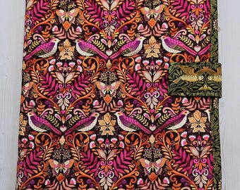 May include: A rectangular fabric book cover featuring a dark brown background with a repeating pattern of pink birds, orange butterflies, and intricate floral foliage. The cover includes a matching fabric strap closure on the right side.
