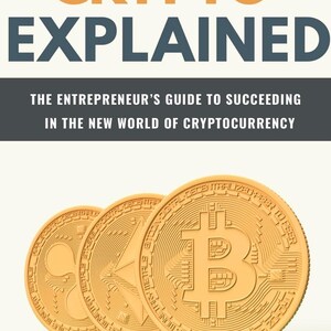 May include: Three gold-coloured cryptocurrency coins, Bitcoin, Ethereum, and Ripple, are arranged in a row on a white background. The coins are all in focus and have a metallic sheen. The text "CRYPTO EXPLAINED" is visible above the coins, and the text "THE ENTREPRENEUR'S GUIDE TO SUCCEEDING IN THE NEW WORLD OF CRYPTOCURRENCY" is visible below the coins.