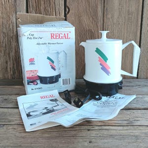 May include: A white electric coffee pot with a black base and a green, pink, and purple abstract design. The coffee pot is labeled "REGAL" and comes with a box and instruction manual.