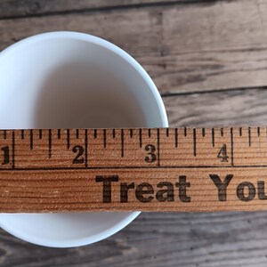 May include: A white ceramic bowl with a wooden ruler measuring its diameter. The bowl is approximately 7.6 cm in diameter. The text "Treat You" is visible on the ruler.
