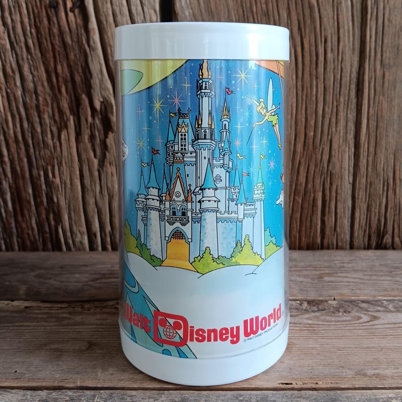 May include: A cylindrical white container with a colourful illustration of Cinderella's castle at Walt Disney World. The design includes Tinkerbell, stars, and the Walt Disney World logo in red.