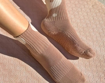 May include: A pair of brown and white patterned socks with grippy dots on the bottom. The socks are made of a soft, comfortable material and are perfect for yoga or other activities.
